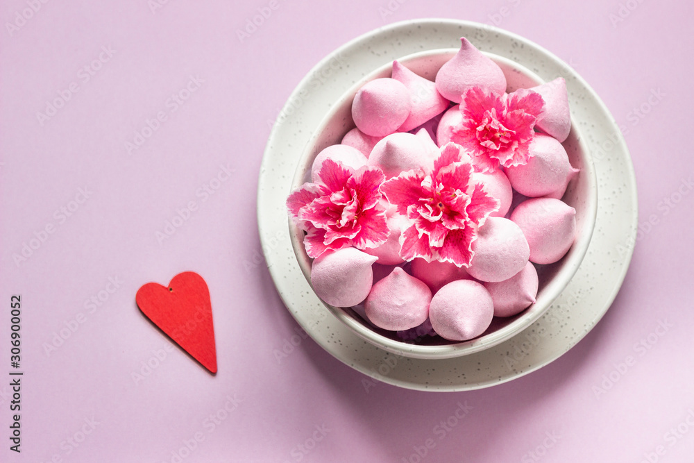 Small meringues and pink flowers in a ceramic bowl on pink paper background. Gift for Valentine's Day. Small meringues and pink flowers in a ceramic bowl on pink paper background. Gift for Valentine's Day.
