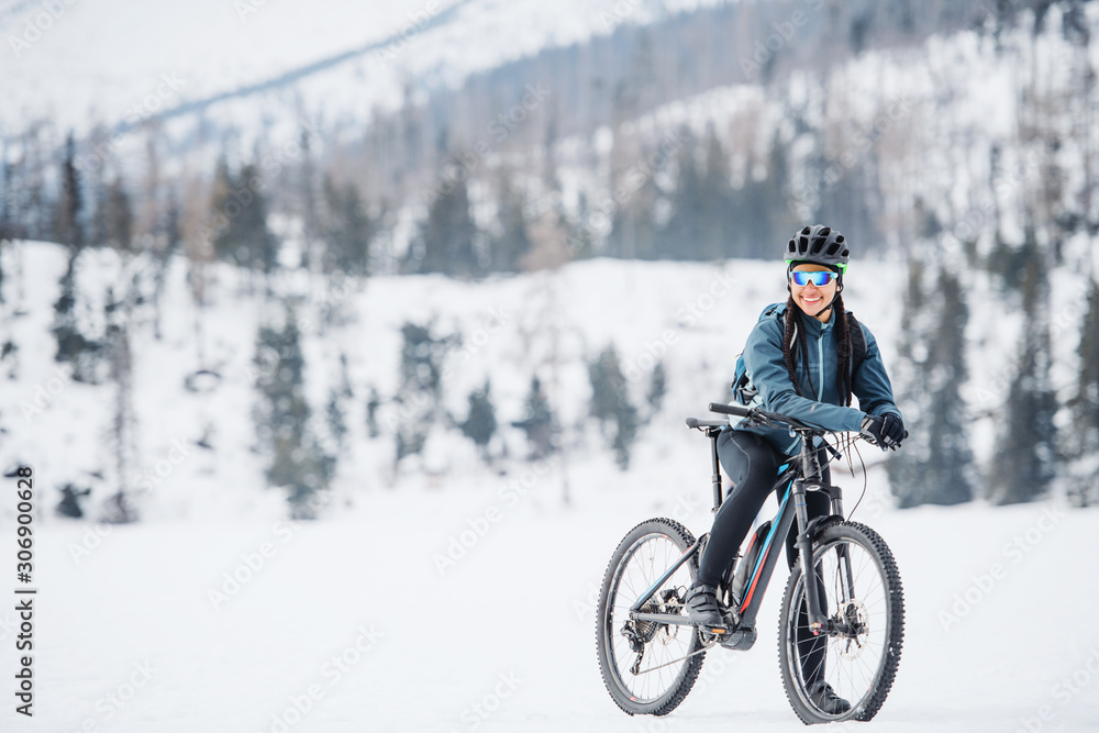 Female mountain biker with bicycle standing outdoors in winter nature.