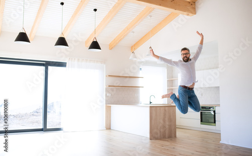 Cheerful mature man moving in new unfurnished house, jumping.