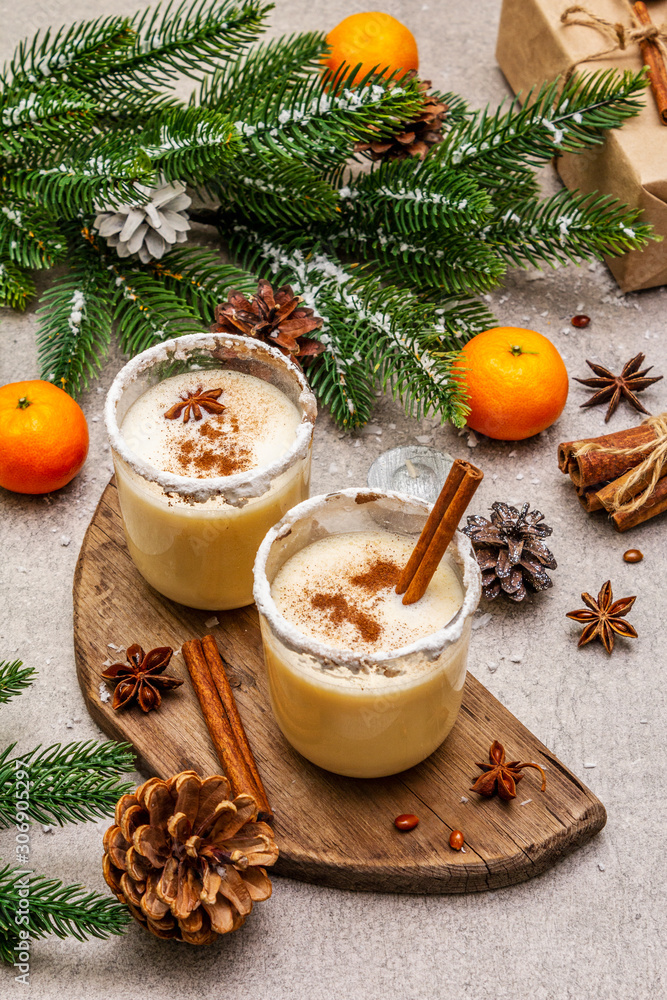 Eggnog with cinnamon and nutmeg for Christmas and winter holidays. Homemade beverage in glasses with spicy rim. Tangerines, candles, gift. Stone concrete background Eggnog with cinnamon and nutmeg for Christmas and winter holidays. Homemade beverage in glasses with spicy rim. Tangerines, candles, gift. Stone concrete background