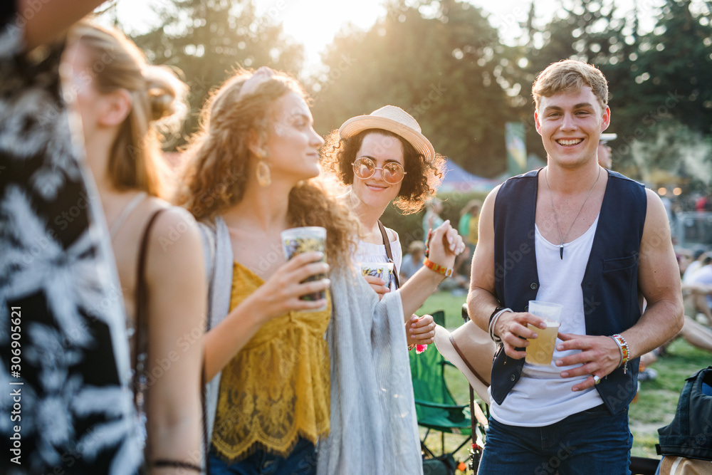 Group of young friends with drinks at summer festival, standing.