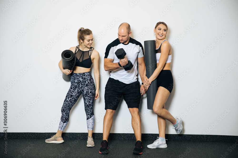 Obraz premium Young sports girls and boy are engaged in fitness, lifestyle, sports and healthy eating, in the gym girls do exercises,On a white background posing in a sports hall