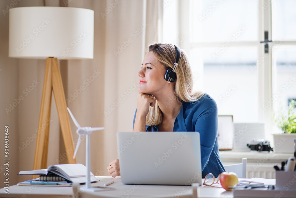 Young woman engineer with headphones sitting at the desk indoors in home office.
