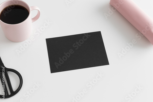Top view of a black card mockup with workspace accessories and a cup of coffee on a white table.