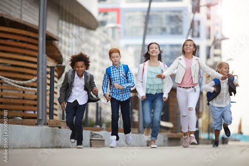Group of multiethnic school children running together along the street after school