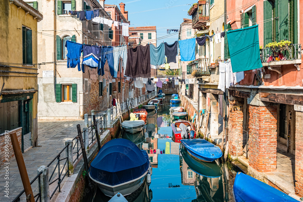 Traditional canal street with reflection in the water laundry hanging out of a typical Venetian facade. Italy