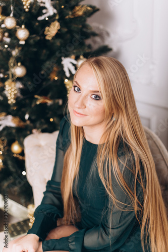 Close up portrait of young sexy beautiful blondie caucasian woman with long hair sitting on sifa near christmas eve in cozy home. Fashion, holidays, christmas concept