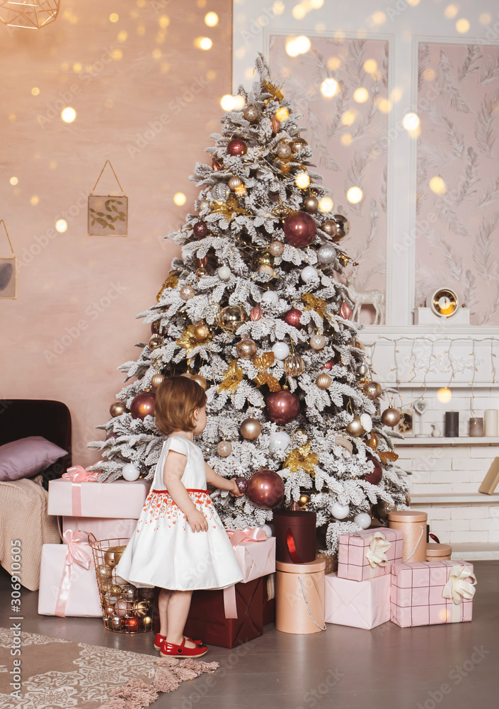 Christmas interior with decorated Christmas tree. A little girl in a white dress from the back. Holiday lights. Christmas interior with decorated Christmas tree. A little girl in a white dress from the back. Holiday lights.