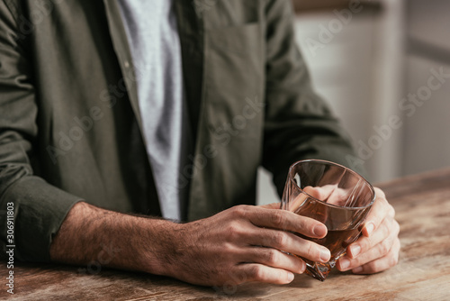 Cropped view of man holding whiskey glass at table