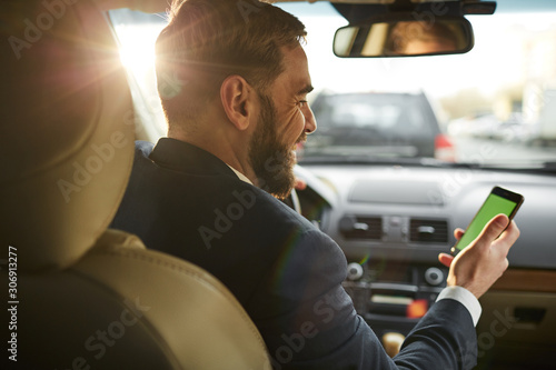 Rear view of bearded young man sitting in the car and holding mobile phone he using online navigator during driving © AnnaStills
