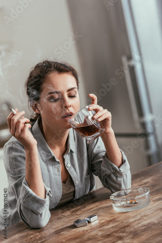 Woman smoking cigarette and holding whiskey glass at table