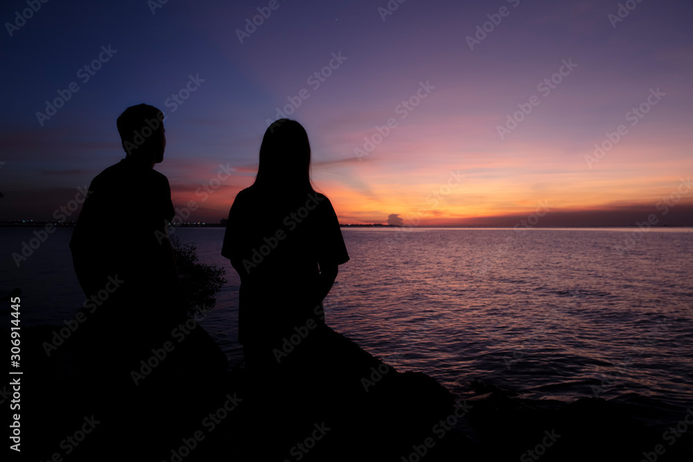 Silhouette A Couple stand looking out to the sea during sunset 