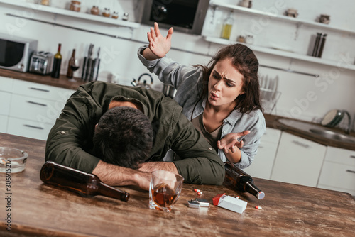Angry woman quarreling with drunk husband with alcohol addiction on kitchen