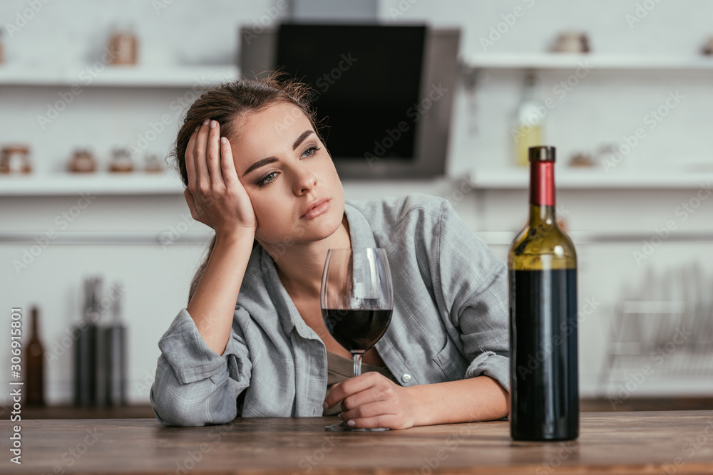 Disappointed woman holding wine glass on kitchen table Disappointed woman holding wine glass on kitchen table