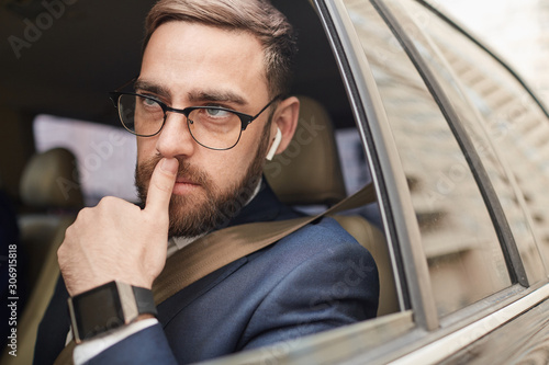 Young businessman in eyeglasses and in suit sitting in the car and thinking about something