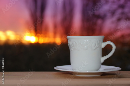 white cup with coffee, tea on a background of dark evening purple sunset among the branches of trees