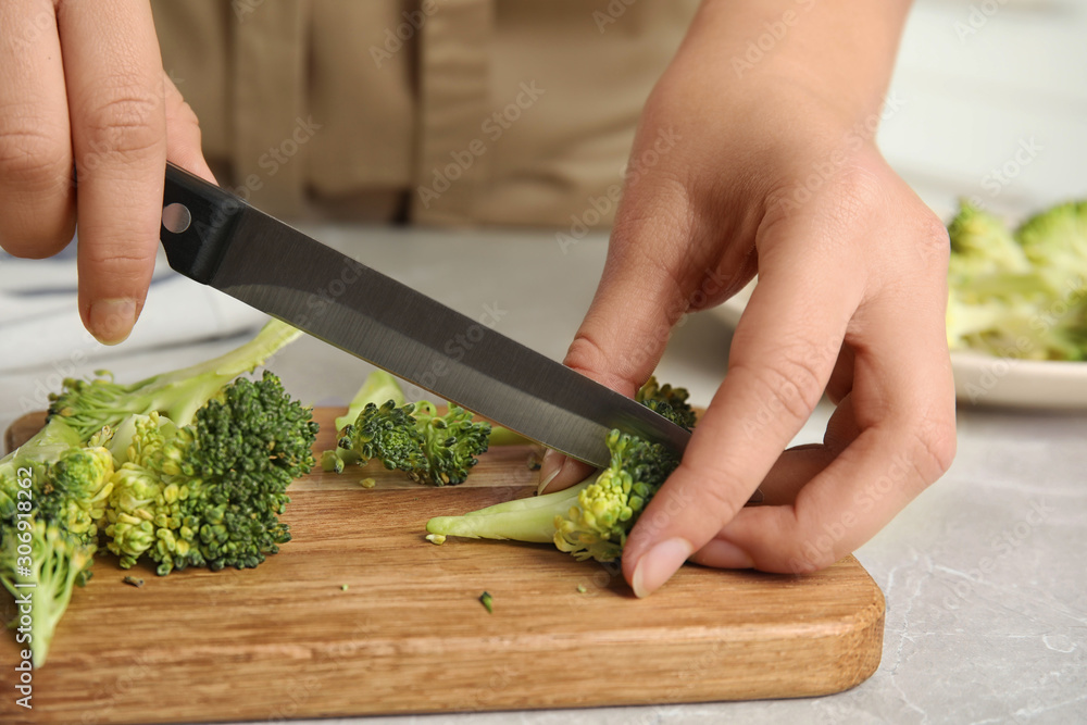 Woman cutting raw broccoli on light grey marble table, closeup