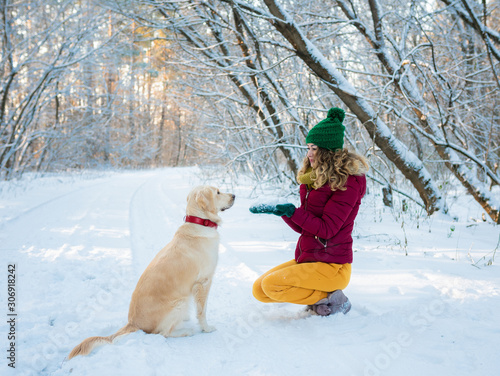 Happy beautiful young woman blowing snowflakes from her hands to her dog golden retriever in a winter day. Friendship, pet and human.