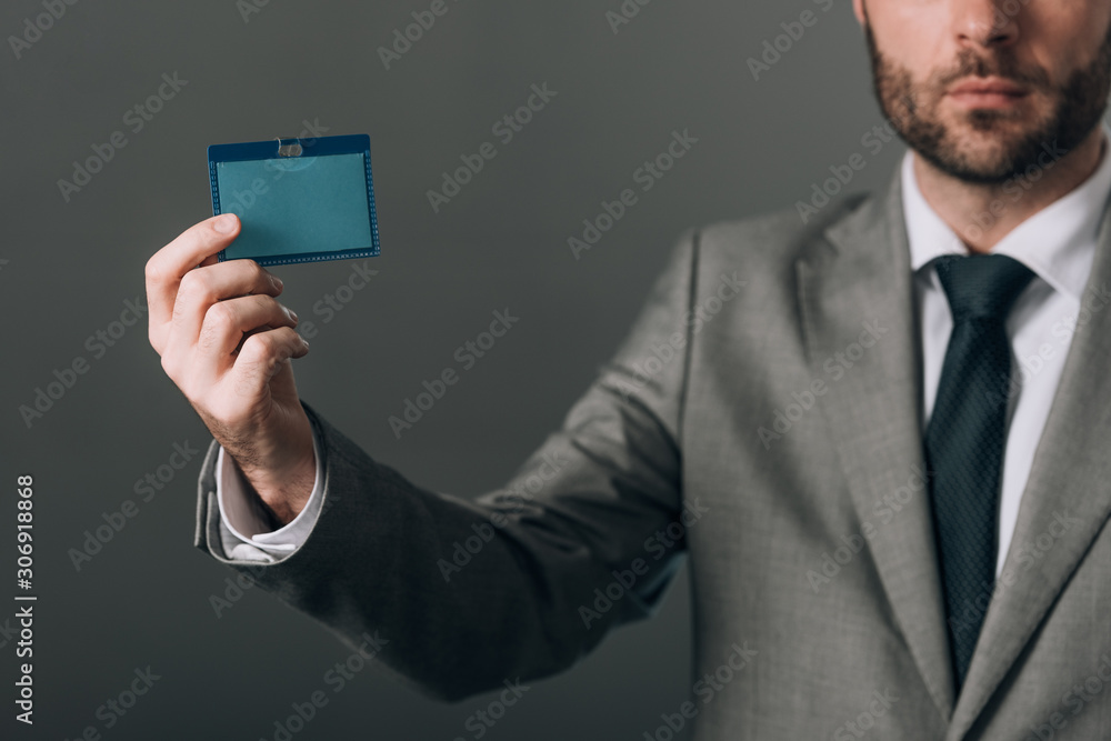 Cropped view of man in suit holding badge with copy space on grey background Cropped view of man in suit holding badge with copy space on grey background