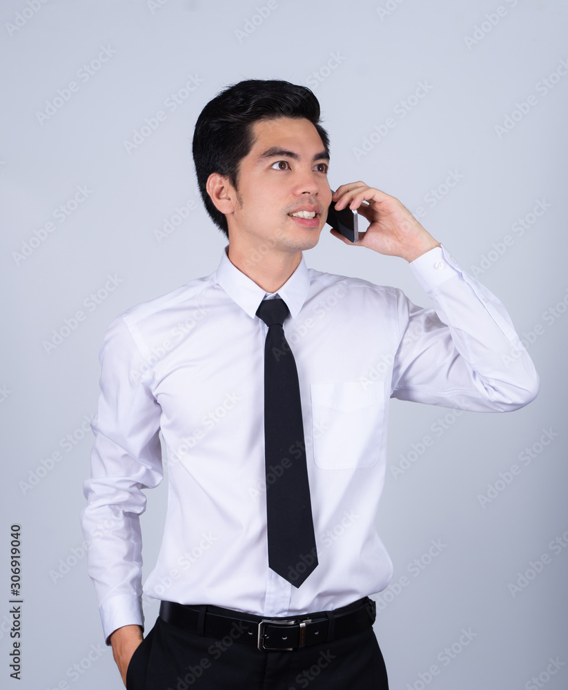 Portrait handsome young asian man wearing a white shirt talking smart phone smile and happy isolated on gray background in studio. Asian man people. business success concept. Portrait handsome young asian man wearing a white shirt talking smart phone smile and happy isolated on gray background in studio. Asian man people. business success concept.