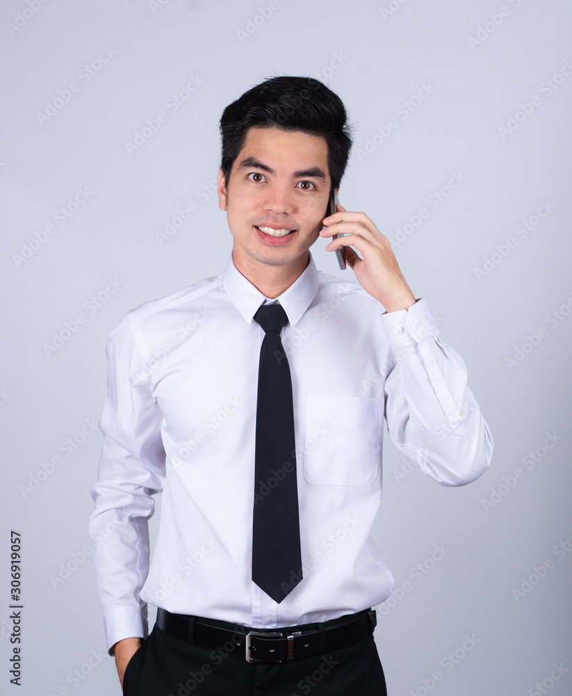 Portrait handsome young asian man wearing a white shirt talking smart phone smile and happy isolated on gray background in studio. Asian man people. business success concept. Portrait handsome young asian man wearing a white shirt talking smart phone smile and happy isolated on gray background in studio. Asian man people. business success concept.