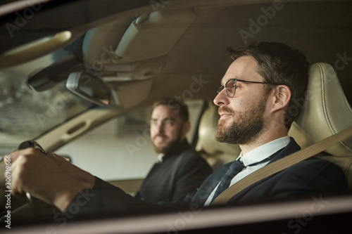 Side view of bearded driver in eyeglasses driving the car with the passenger sitting near by him