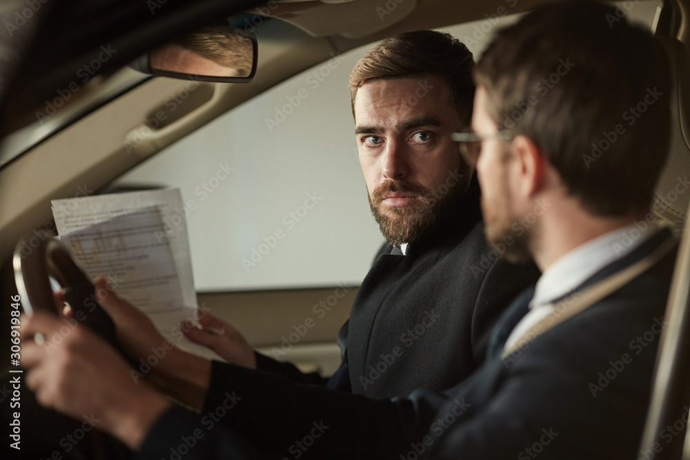 Young bearded man holding contract and talking to other man about the purchase of the car Young bearded man holding contract and talking to other man about the purchase of the car