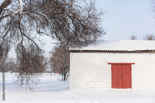 White windowless building with a red door. Winter in the village © Kate