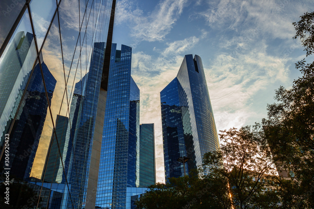 Obraz premium Skyscraper glass facades on a bright sunny day with sunbeams in the blue sky. Modern buildings in business district. Economy, finances, business activity concept. Bottom up view 