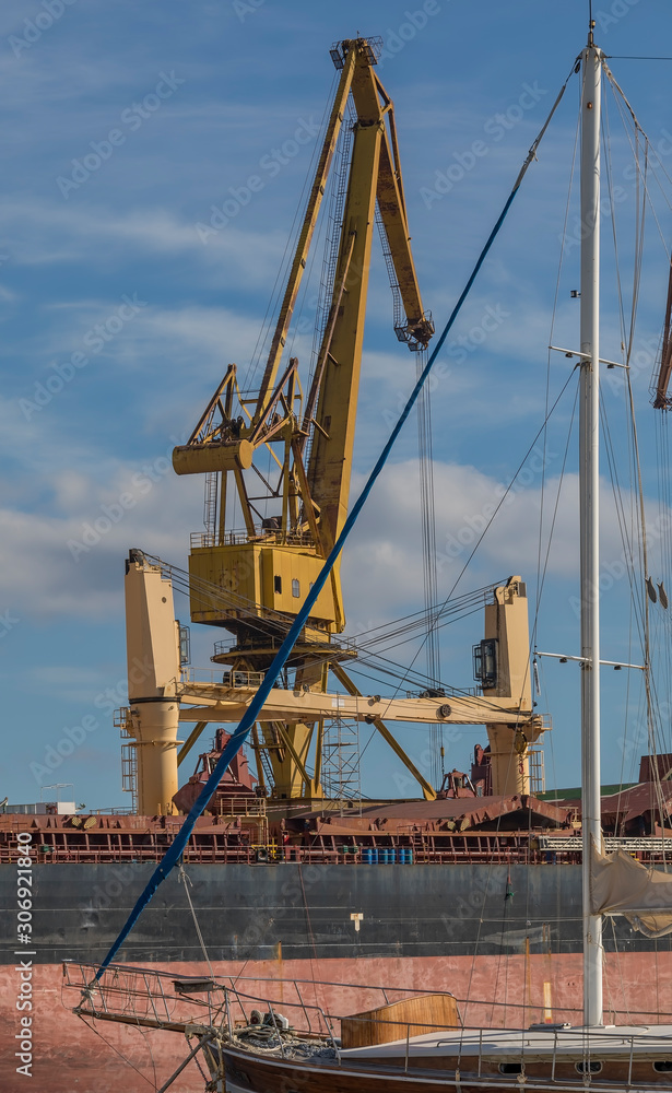 Industrial Crane. Big yellow crane with sailboat in the front of photo and sky with clouds in the background. Stock image.