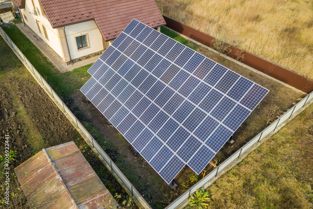 Aerial view of big blue solar panel installed on ground structure near private house.