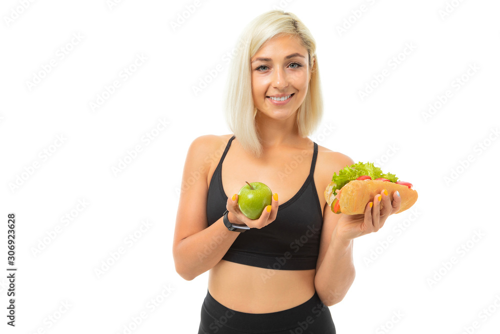 sports girl in a sports uniform shows an apple and fast food on a camera on a white background sports girl in a sports uniform shows an apple and fast food on a camera on a white background