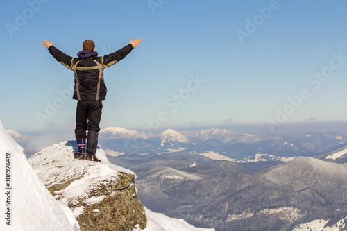 Silhouette of alone tourist standing on snowy mountain top in winner pose with raised hands enjoying view and achievement on bright sunny winter day. Adventure, outdoors activities, healthy lifestyle. © bilanol