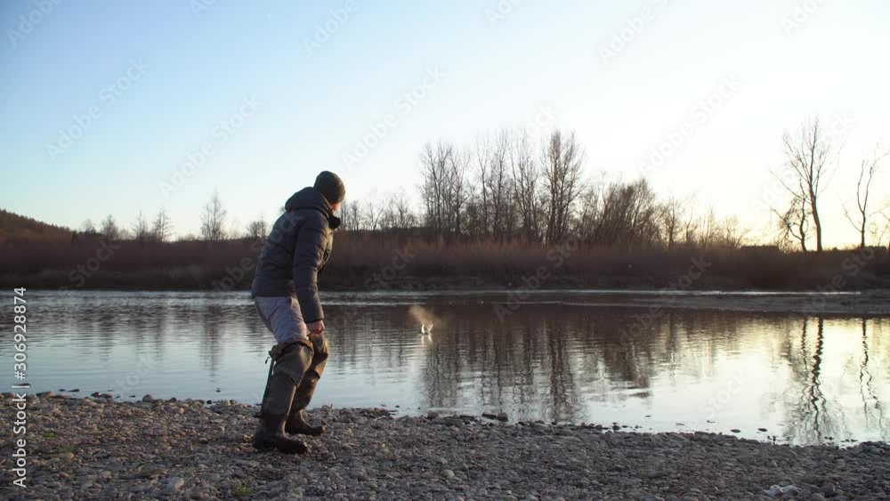 Young guy throws stones on the water.The rock jumps on the water.Entertainment on the bank of the river Young guy throws stones on the water.The rock jumps on the water.Entertainment on the bank of the river