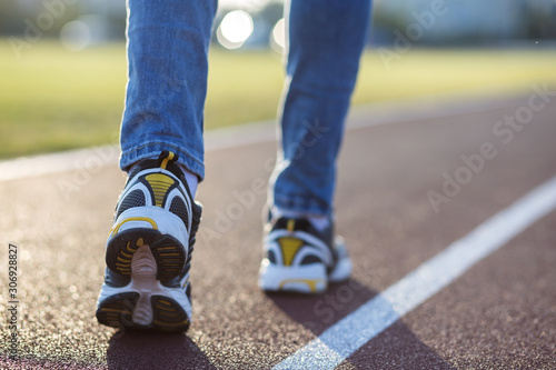 Close up of woman feet in sport sneakers and blue jeans on running lane on outdoor sports court.