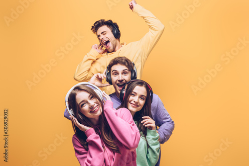 smiling friends listening music in headphones and dancing together, isolated on yellow photo