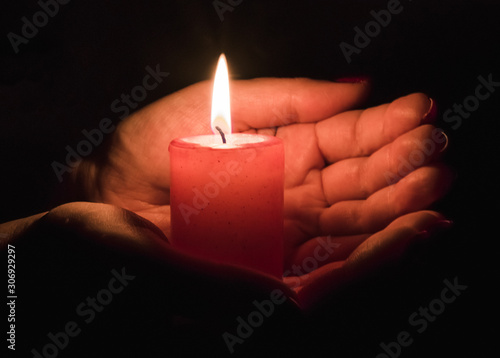  Female hands holding a burning candle in the dark