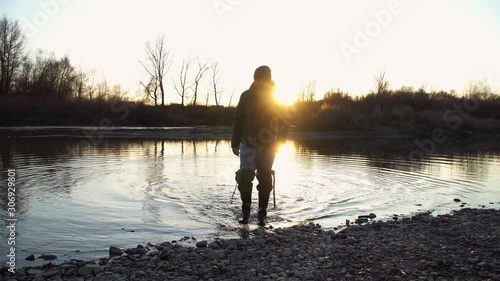 A man comes out of the water at sunset. Behind the fisherman, sunbeams break through, glare of the sun