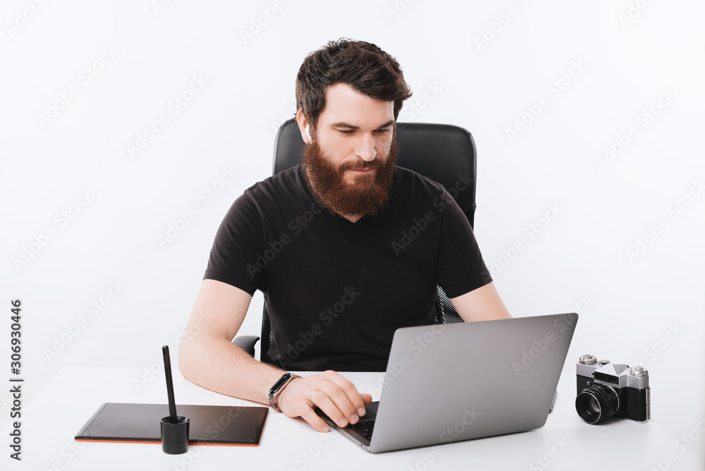 Bearded young man is looking at computer on his desk. Bearded young man is looking at computer on his desk.