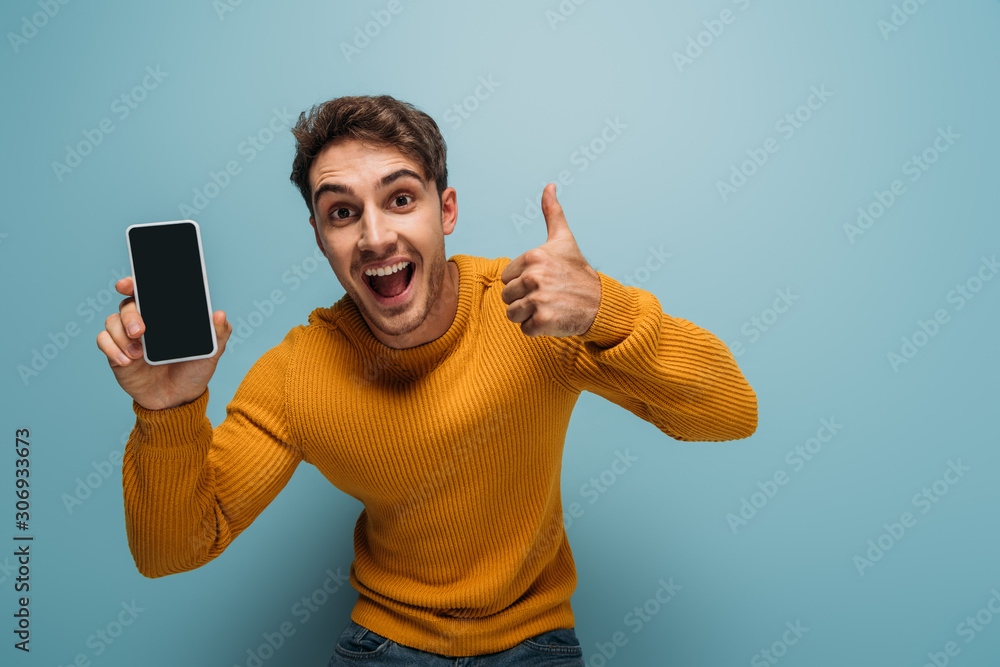 excited man showing thumb up and smartphone with blank screen, isolated on blue excited man showing thumb up and smartphone with blank screen, isolated on blue