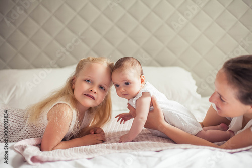 Young beautiful mother holds a baby. Little sister kisses her little sister. Baby. Children bedroom.