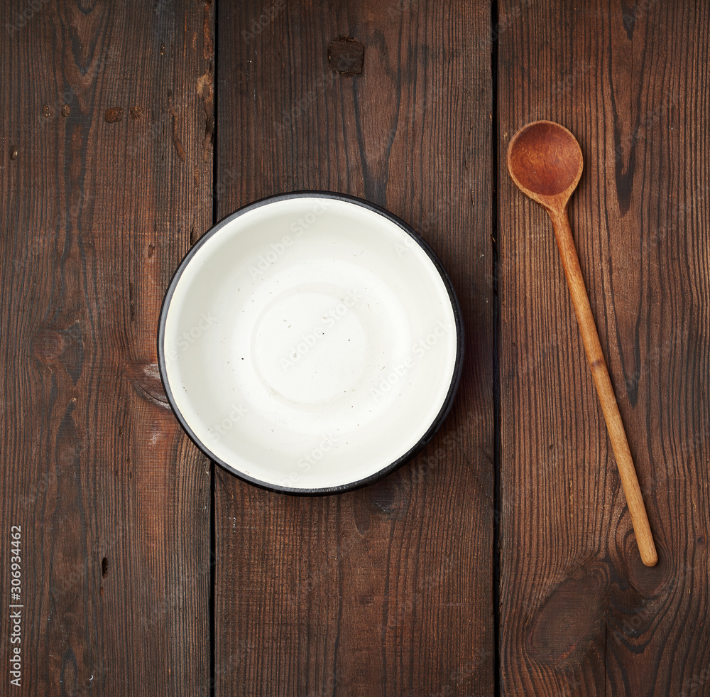empty round metal white plate and wooden spoon on the table empty round metal white plate and wooden spoon on the table