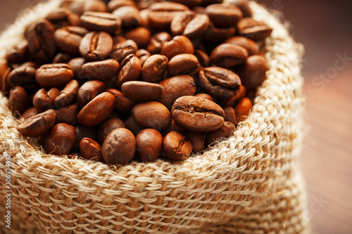 Coffee beans closeup in burlap bag on wooden background.