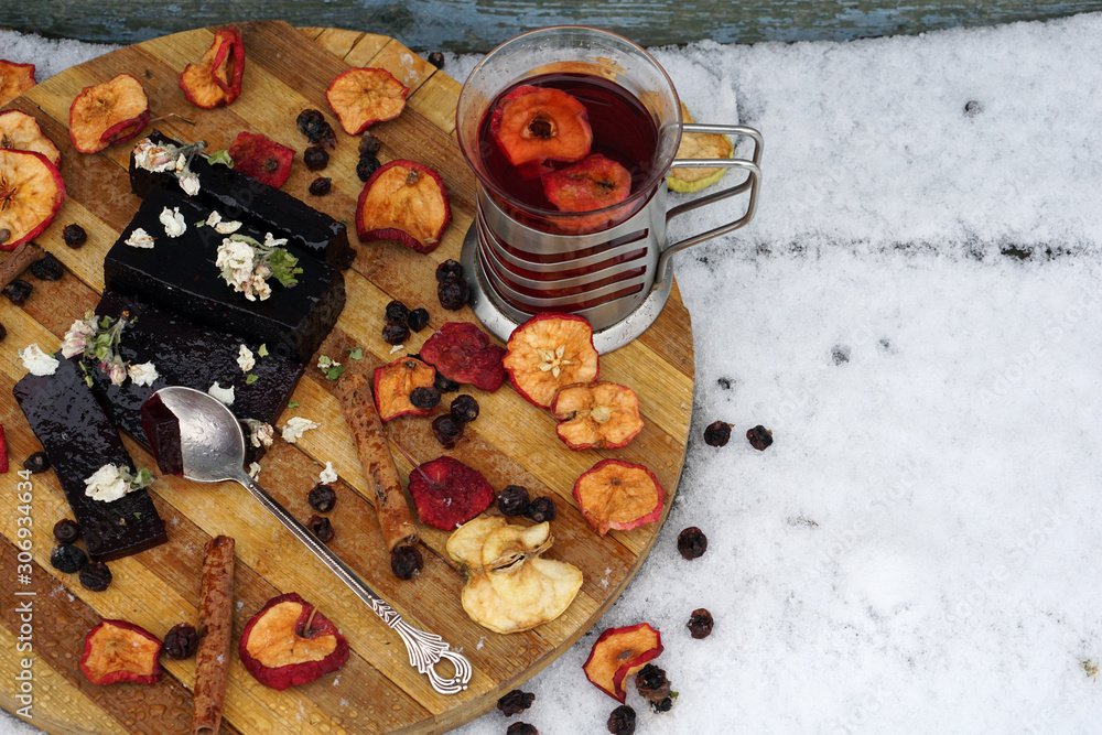 Tea party   with cup of hot tea,  fruit jelly,  dry apple, berry of black chokeberry, cinnamon on wooden plate in garden