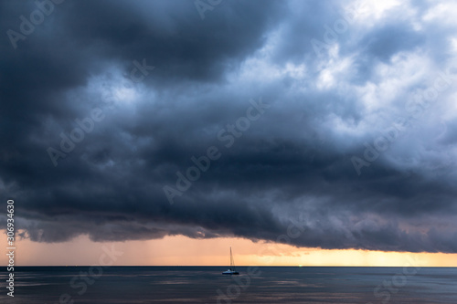 Storm coming lead scary cloud in dark mode with strong wind on the sky over the ocean, one yacht boat alone on the sea