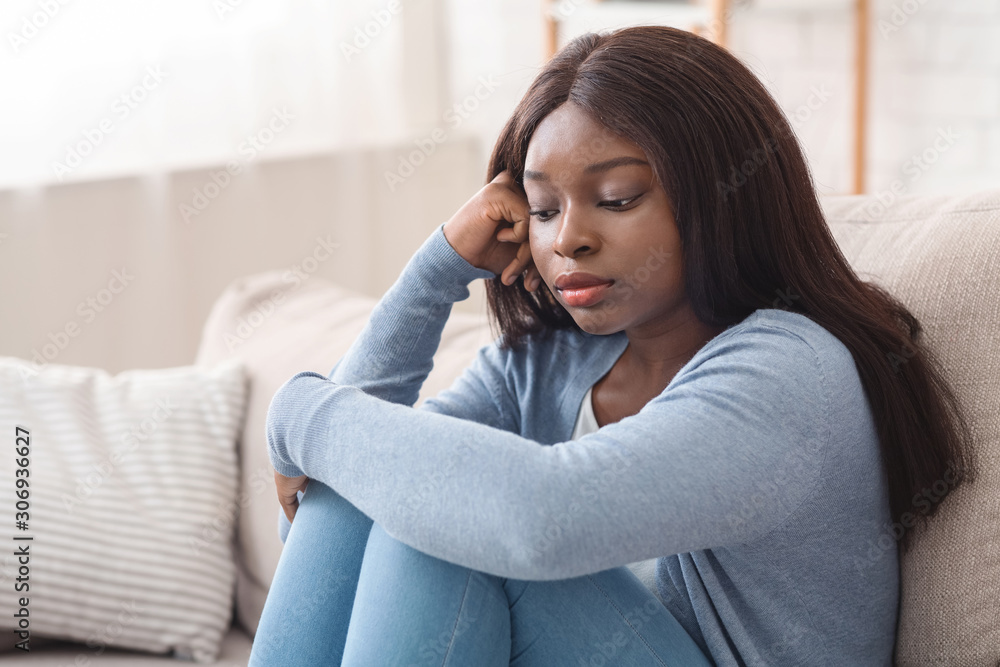 Upset black girl sitting on couch with thoughtful face expression Upset black girl sitting on couch with thoughtful face expression