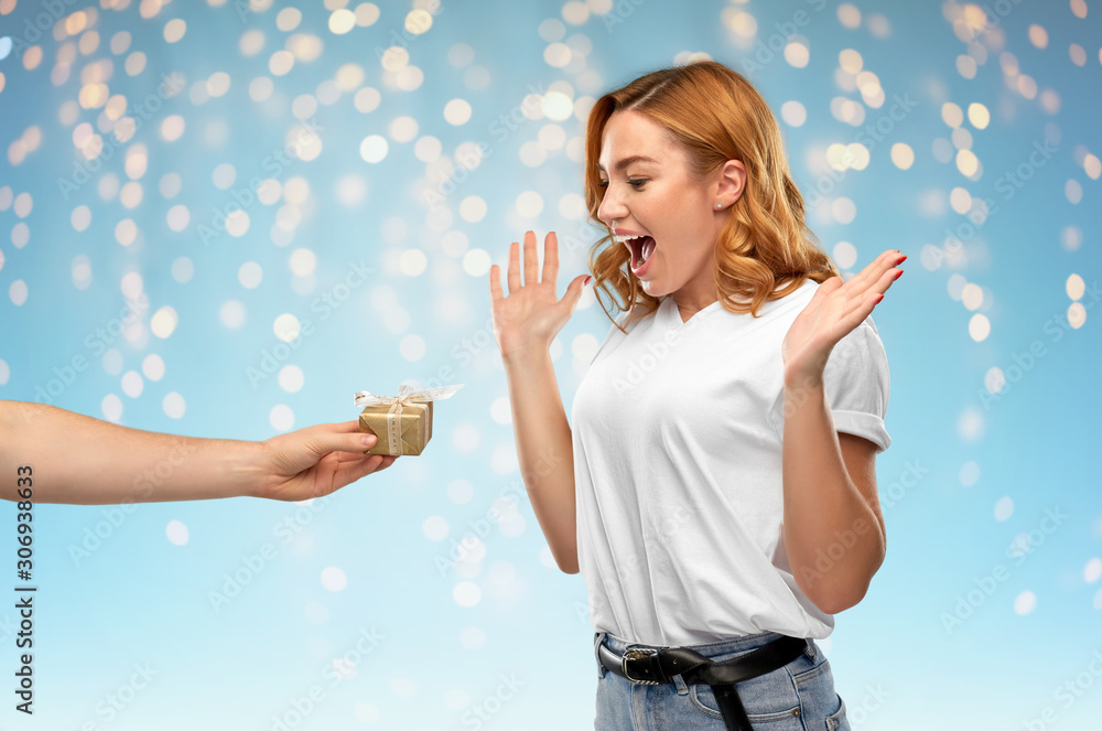 holiday, christmas and valentine's day concept -happy woman in white t-shirt receiving little gift box from man over holidays lights on blue background holiday, christmas and valentine's day concept -happy woman in white t-shirt receiving little gift box from man over holidays lights on blue background
