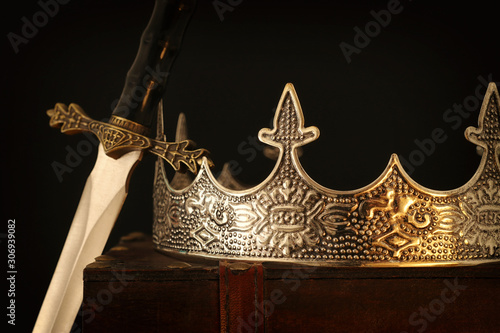 low key image of beautiful queen/king crown over antique box next to sword. fantasy medieval period. Selective focus