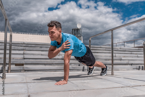 Male athlete training abdominal muscle press, workout training, summer in city. Fitness motivation youth lifestyle. Sportswear, shorts and a T-shirt in sneakers. Cloud stair background.
