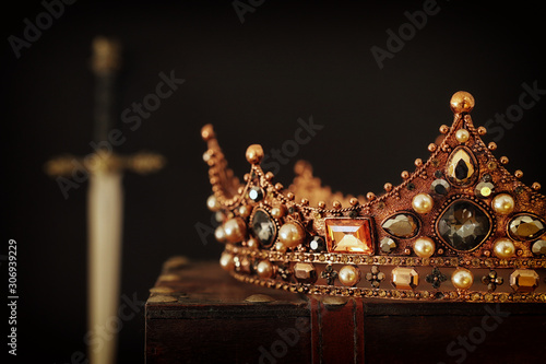 low key image of beautiful queen/king crown over antique box next to sword. fantasy medieval period. Selective focus